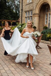 A woman in a white wedding dress is assisted by another woman in a black dress as they prepare for a wedding at Woodlands Hotel, Leeds