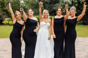 A bride in a white strapless gown stands with four bridesmaids in black dresses at Woodlands Hotel, Leeds