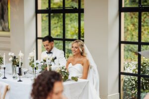 A bride in a strapless white gown and veil sits at a table with a man in a white suit and bow tie at Woodlands Hotel, Leeds