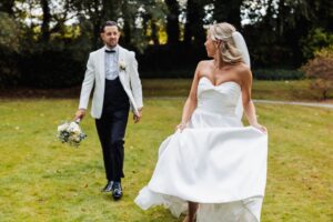 A bride in a strapless white gown and a groom in a white tuxedo walk across a grassy field at Woodlands Hotel, Leeds