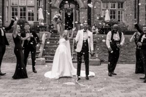 Confetti falls as the bride and groom are surrounded by guests in formal attire, celebrating their wedding exit at Woodlands Hotel, Leeds