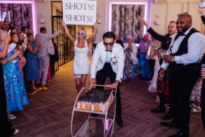 A man in a white suit and sunglasses pushes a trolley filled with small bottles at Woodlands Hotel, Leeds
