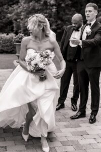 A bride in a strapless wedding gown holds a bouquet of flowers, walking on a paved path