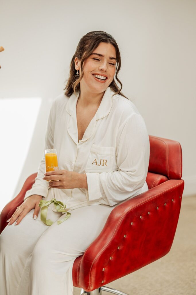 A woman in a white robe with 'AJR' embroidered on the pocket sits on a red leather chair at Autumn & Sam - Owen house barn