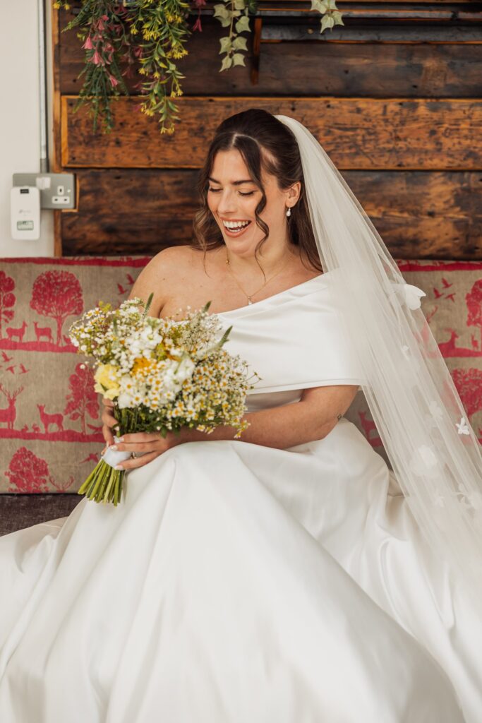 A bride in a white wedding dress and veil holds a bouquet of wildflowers at Autumn & Sam - Owen house barn