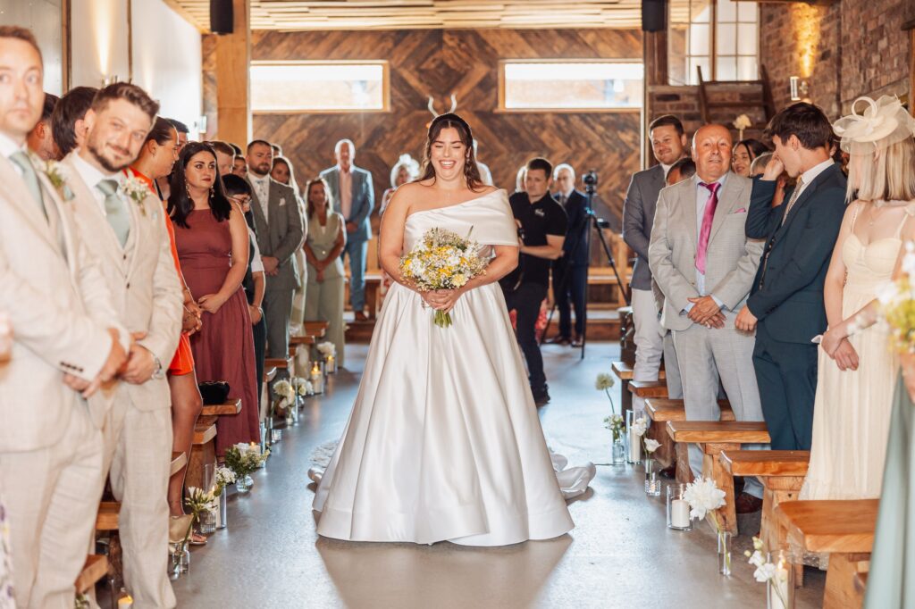 A bride in a white wedding dress walks down the aisle, holding a bouquet of flowers, accompanied by an older man in a dark suit