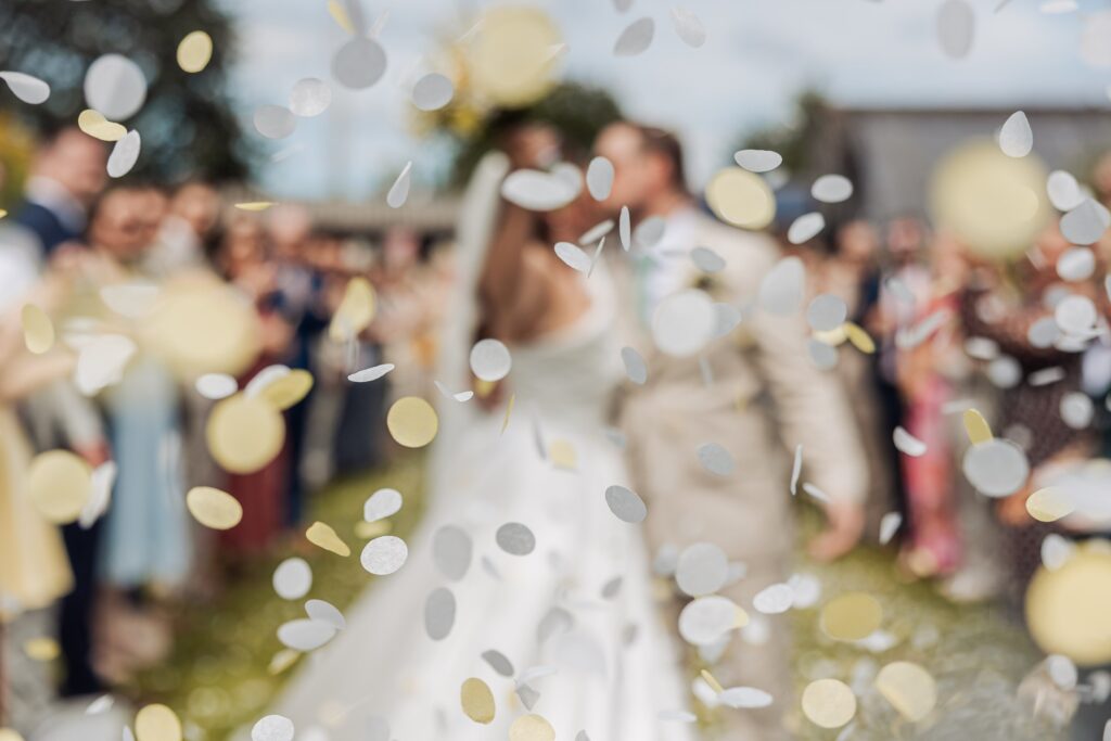 Confetti falls as a couple in wedding attire celebrates their exit, surrounded by guests in formal attire at Autumn & Sam - Owen house barn