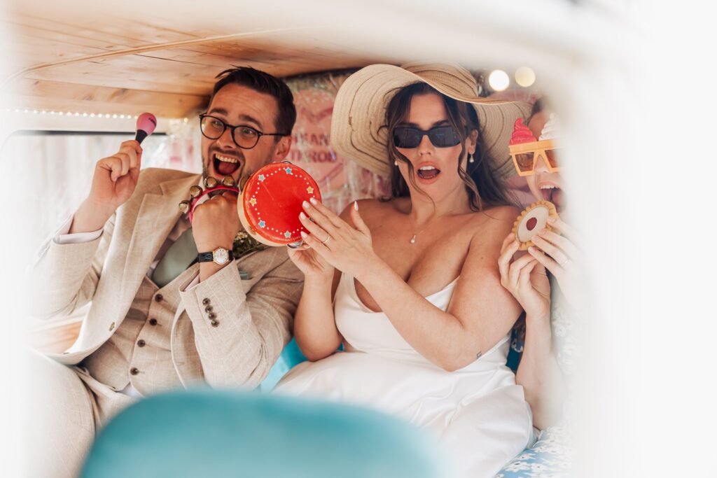 A couple in wedding clothes enjoys a musical moment inside a vehicle or tent, holding tambourines and a maraca