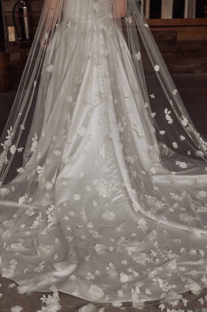 A close-up of a wedding dress with a full skirt adorned with white floral appliqués at Autumn & Sam - Owen house barn