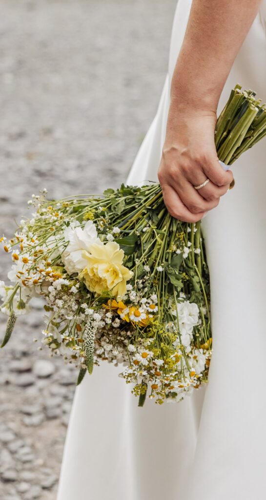 A hand holding a bouquet of wildflowers, including white and yellow blooms, with green foliage