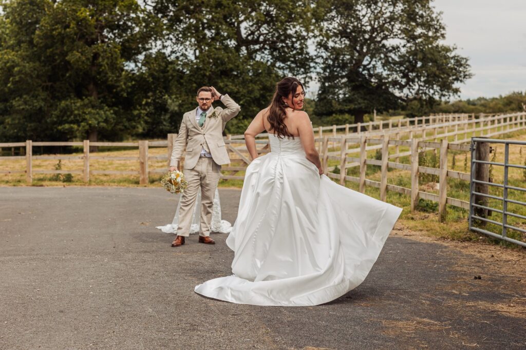 A bride in a white gown twirls as a groom in a beige suit walks behind her, holding a bouquet at Autumn & Sam - Owen house barn