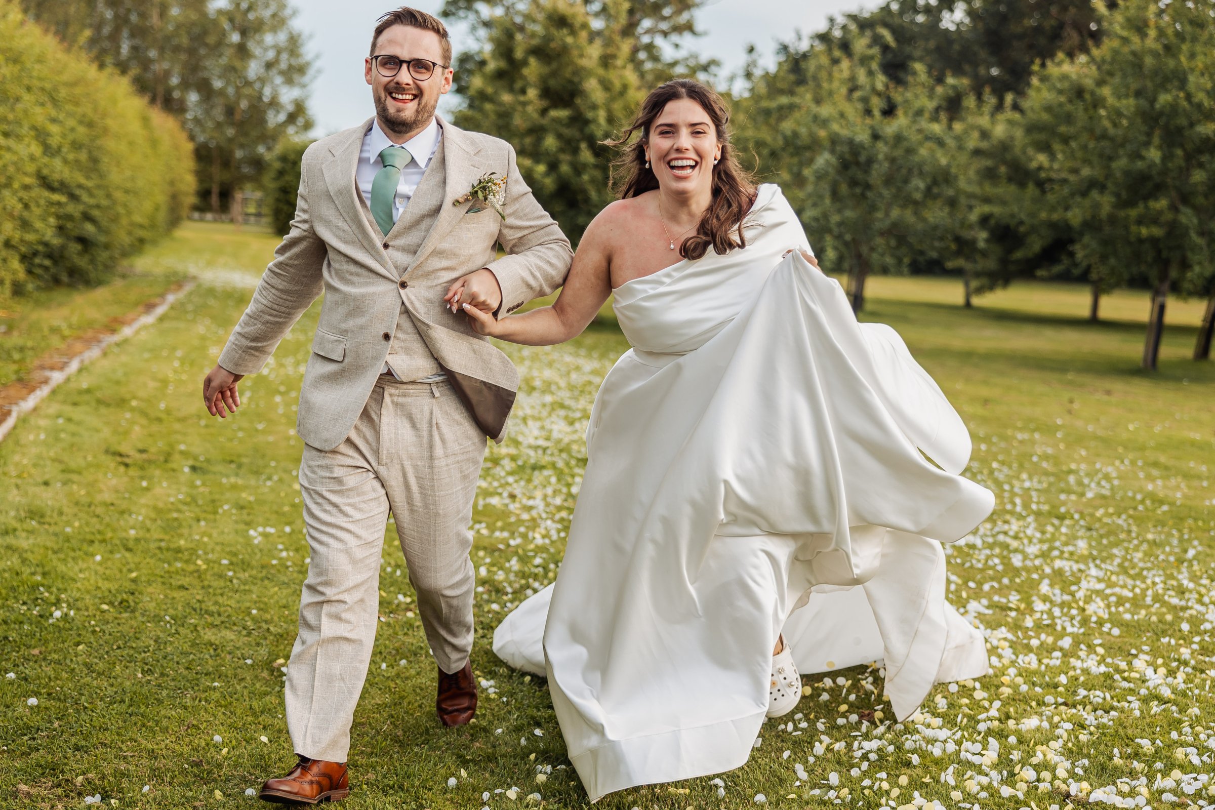 Bride and groom running hand in hand across the daisy-covered lawn at Owen House Wedding Barn