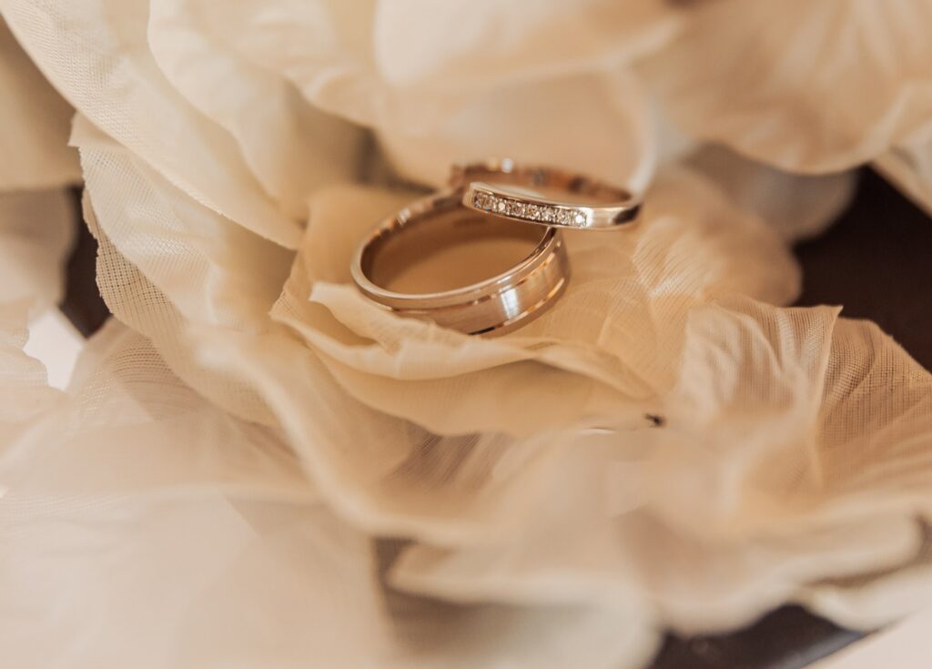 Two wedding rings with a diamond band are placed on a delicate, ruffled fabric at Colshaw Hall, Cheshire
