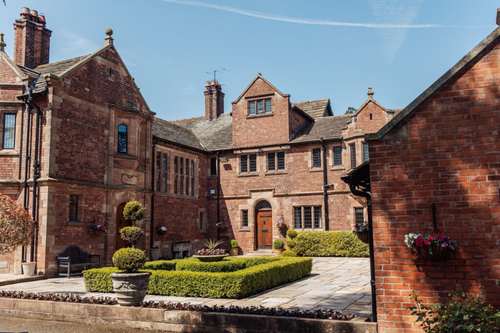 A red-brick building with a central courtyard, neatly trimmed hedges, and hanging baskets, under a clear blue sky at Colshaw Hall, Cheshire