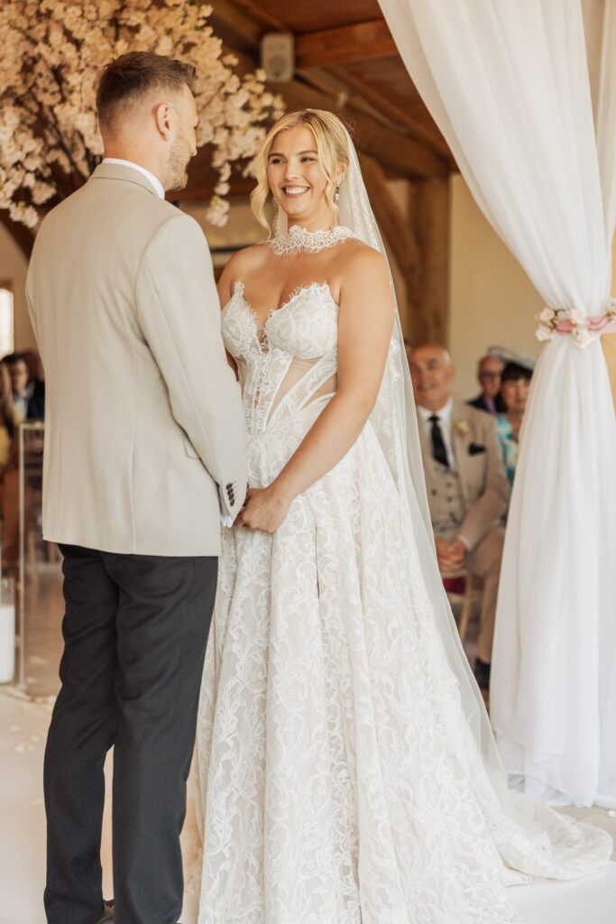 A couple stands close together in a warmly lit wooden hall during a wedding ceremony
