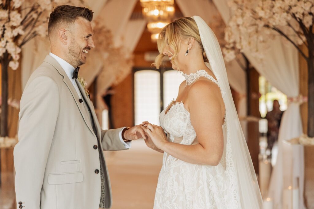 A couple exchanging rings during a wedding ceremony in an indoor venue with decorative elements