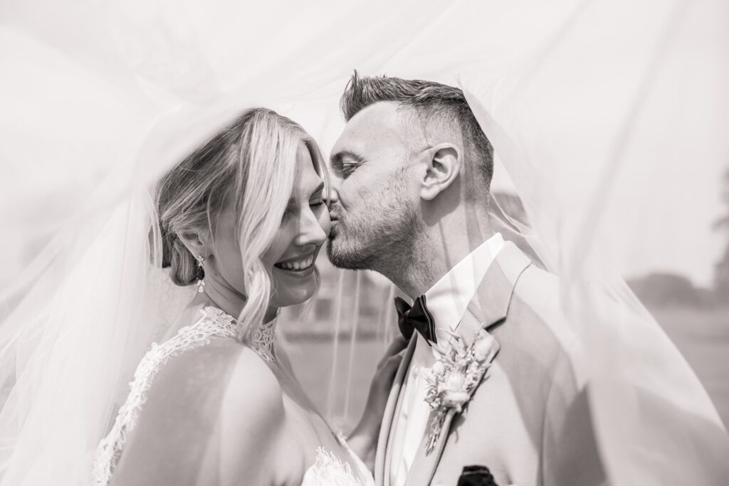 A couple in wedding attire, the bride in a white gown and veil, and the groom in a suit with a boutonniere, are close together at Colshaw Hall, Cheshire