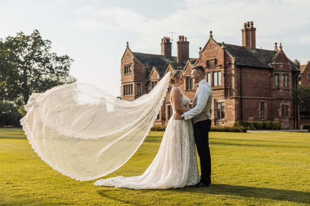 Bride and groom standing on the lawn in front of the red brick facade of Colshaw Hall