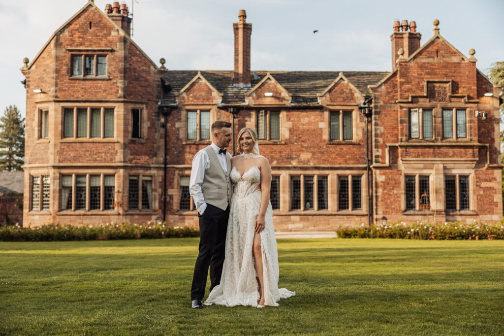 Bride's veil fanned out across the lawn in front of Colshaw Hall as the couple embrace