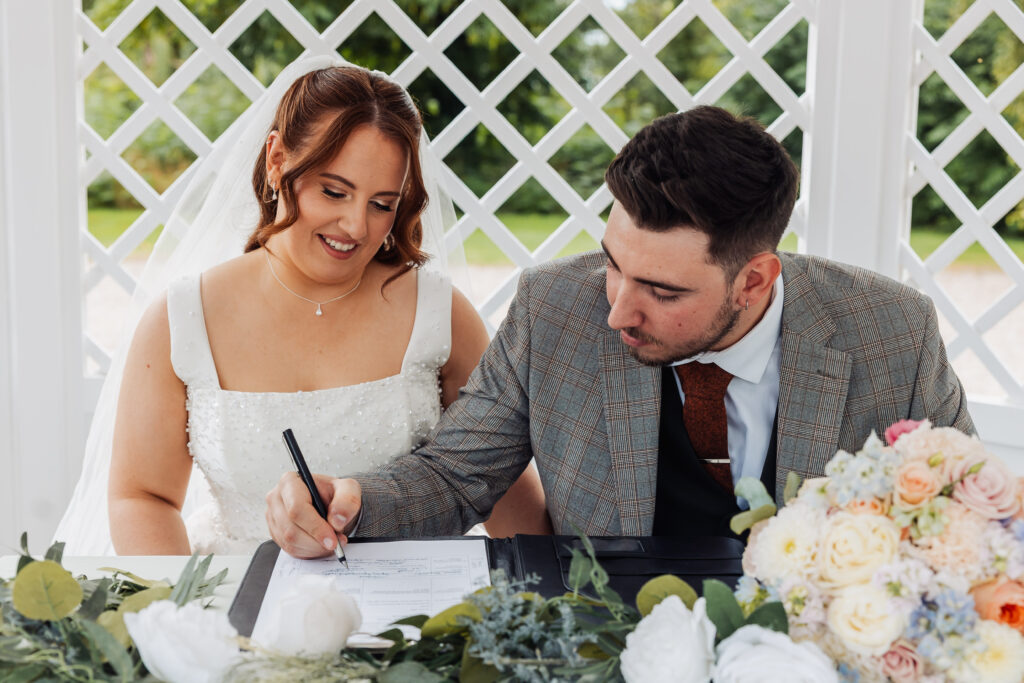 Bride and groom signing the register outdoors at Hodsock Priory