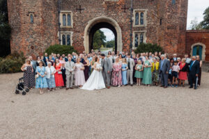 Full wedding group photograph in front of the red-brick Tudor gatehouse at Hodsock Priory