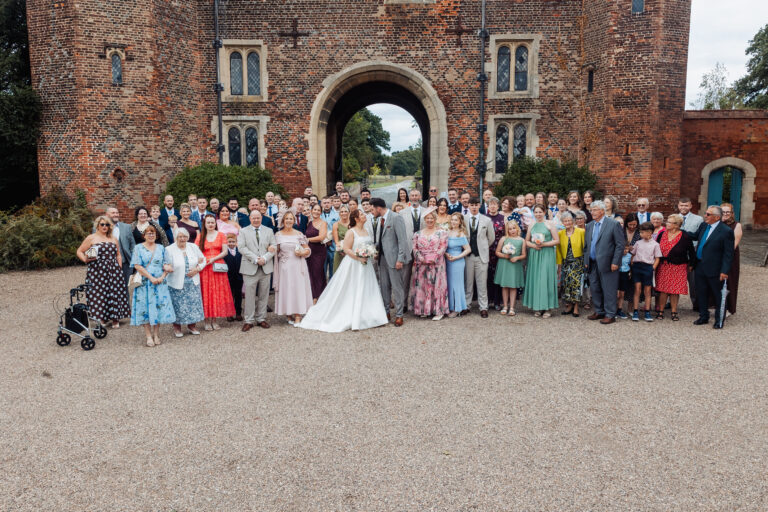 Full wedding group photograph in front of the red-brick Tudor gatehouse at Hodsock Priory