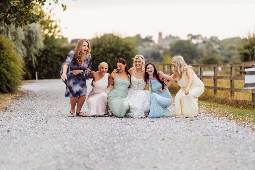 Bride crouching on the path with her bridesmaids at Sedgewell Barn