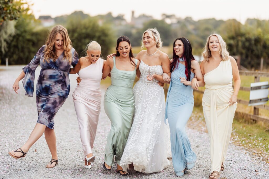 Bride walking arm in arm with her bridesmaids along the drive at Sedgewell Barn