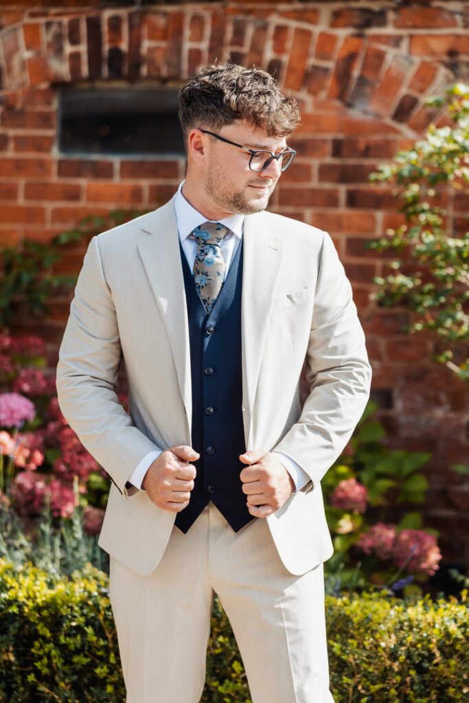 Groom adjusting his cream jacket outside the brick barn at Sedgewell Barn