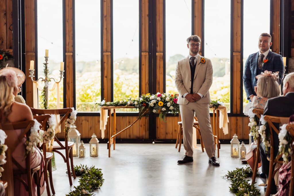 Groom waiting at the front of the Celebration Barn at Sedgewell Barn, daylight flooding through the full glass wall