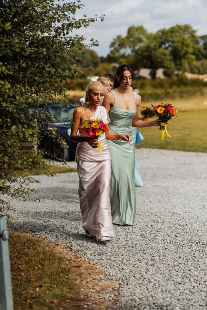 Bridesmaids walking along the path to the barn carrying their bouquets