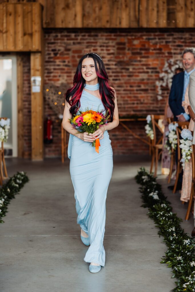 Bridesmaid walking down the aisle inside the barn at Sedgewell Barn