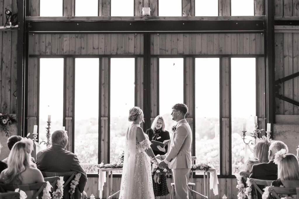 Black and white photograph of the couple at the ceremony against the glass wall of the barn