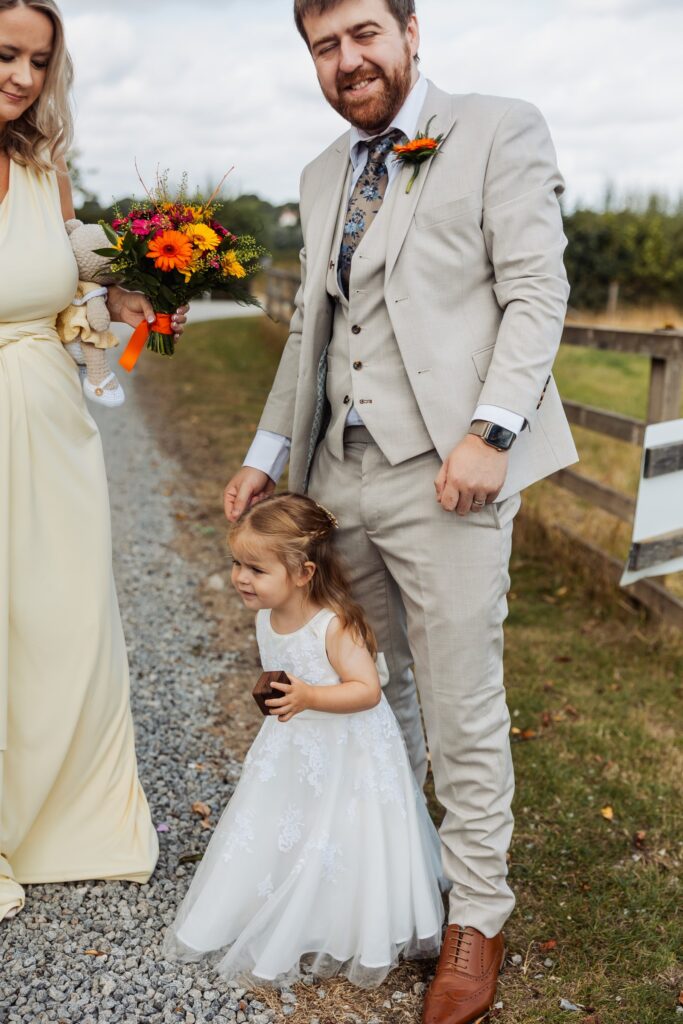 Groom holding hands with a flower girl outside the barn