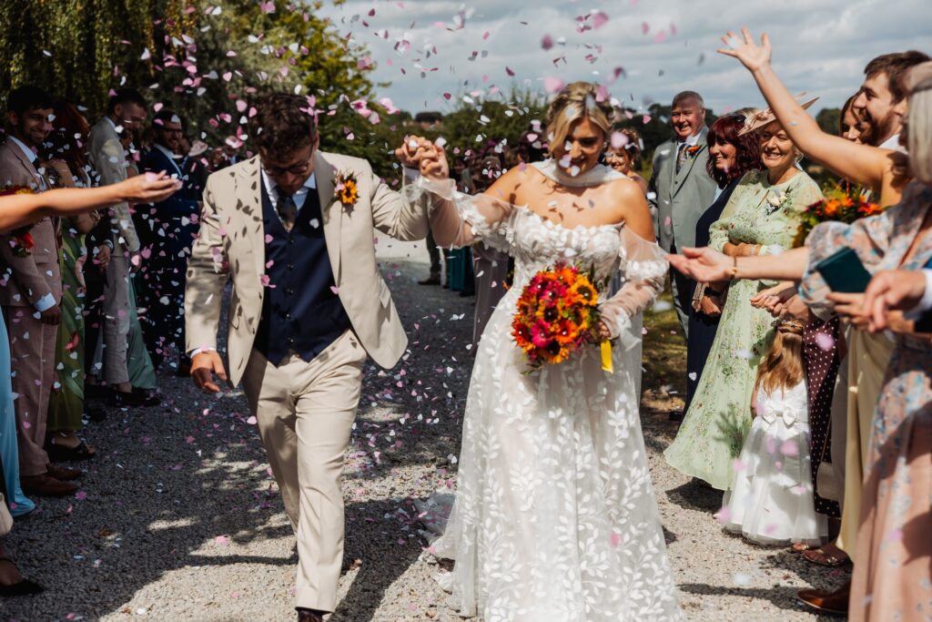 Confetti thrown over the bride and groom as they walk between guests at Sedgewell Barn