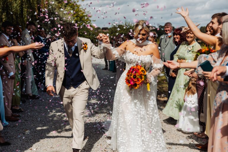 Confetti thrown over the bride and groom as they walk between guests at Sedgewell Barn