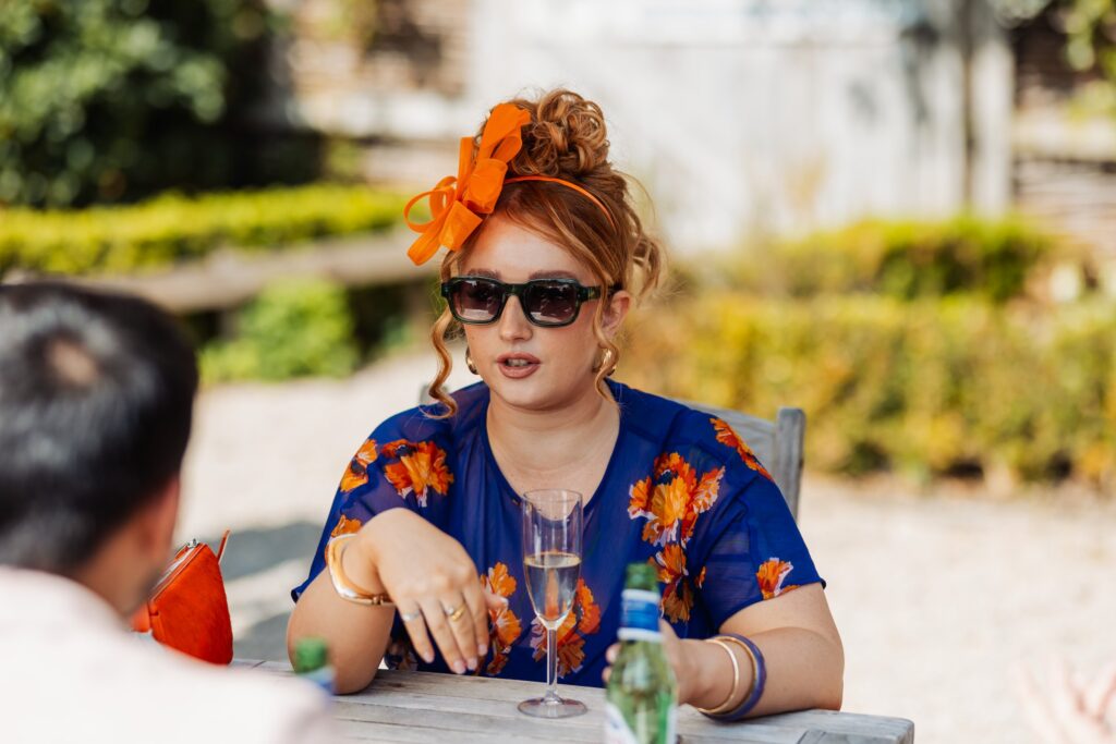 Guest in an orange fascinator seated at a table during the reception