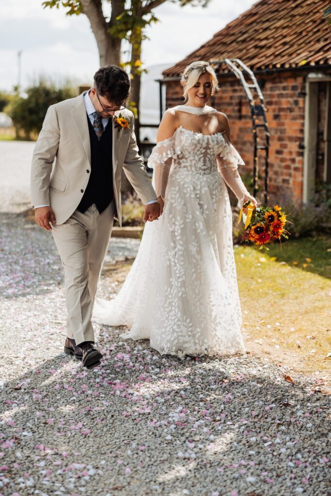 Bride and groom walking away together, her train trailing on the gravel