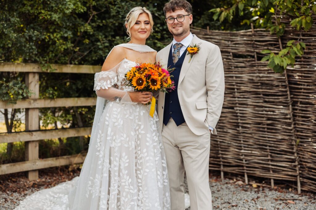 Bride and groom standing by a woven willow fence at Sedgewell Barn