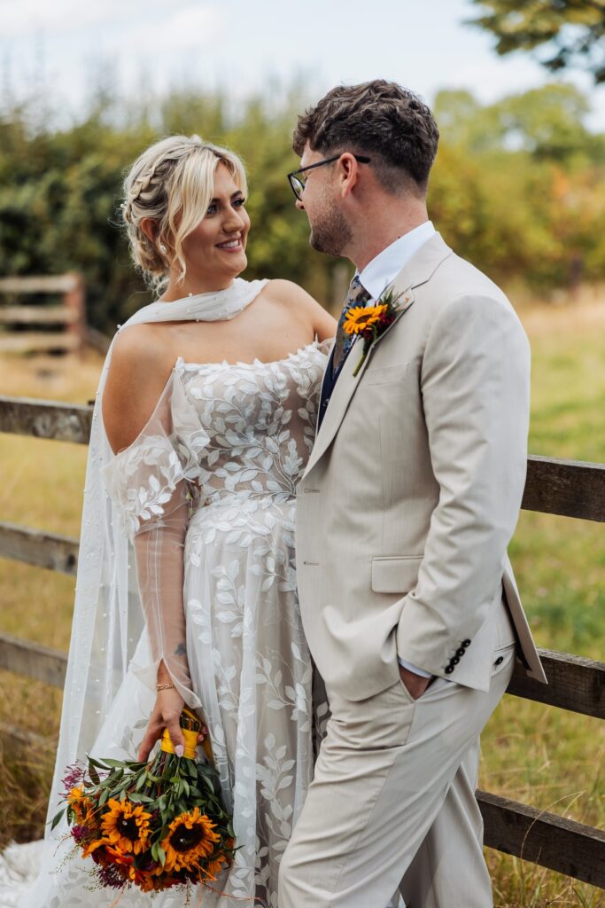 Bride and groom face to face beside a wooden fence at Sedgewell Barn