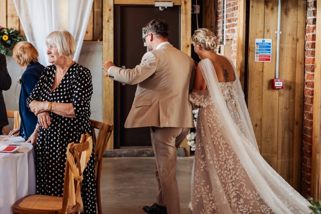 Groom guiding the bride through the barn doorway, her long train behind her