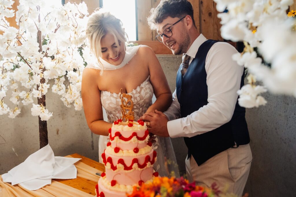 Bride and groom cutting their red and white tiered wedding cake at Sedgewell Barn