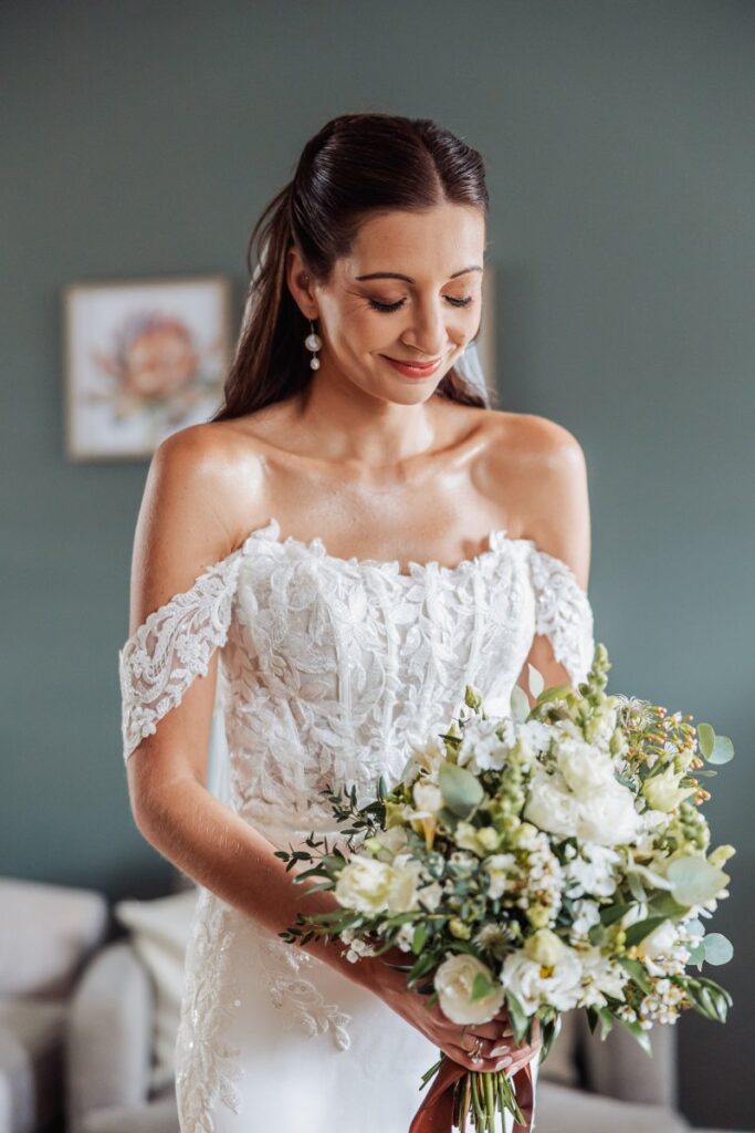 The bride looks down at her bouquet of white roses and eucalyptus in the quiet moments before her Clayfield Farm ceremony.