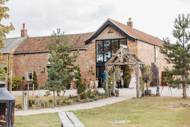 The red brick barns and oak porch at Clayfield Farm near Pocklington, with guests gathering on the gravel before the ceremony.