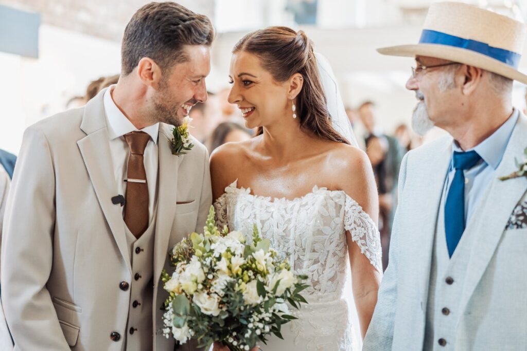 The newly married couple share a look after their ceremony, the groom in a stone three-piece suit with a brown tie.