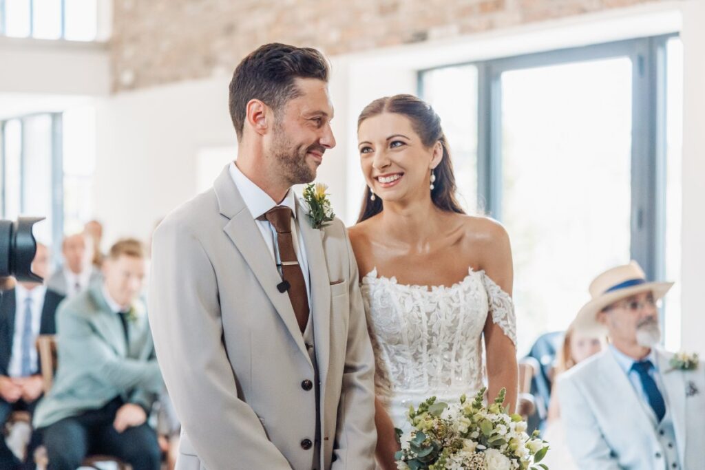 Bride and groom during the ceremony at Clayfield Farm, framed by the exposed brick and tall windows of the barn.