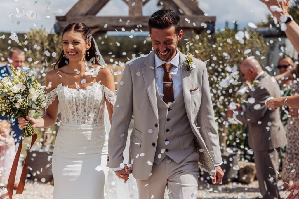 Confetti falls over the newlyweds as they walk out through the oak porch at Clayfield Farm.