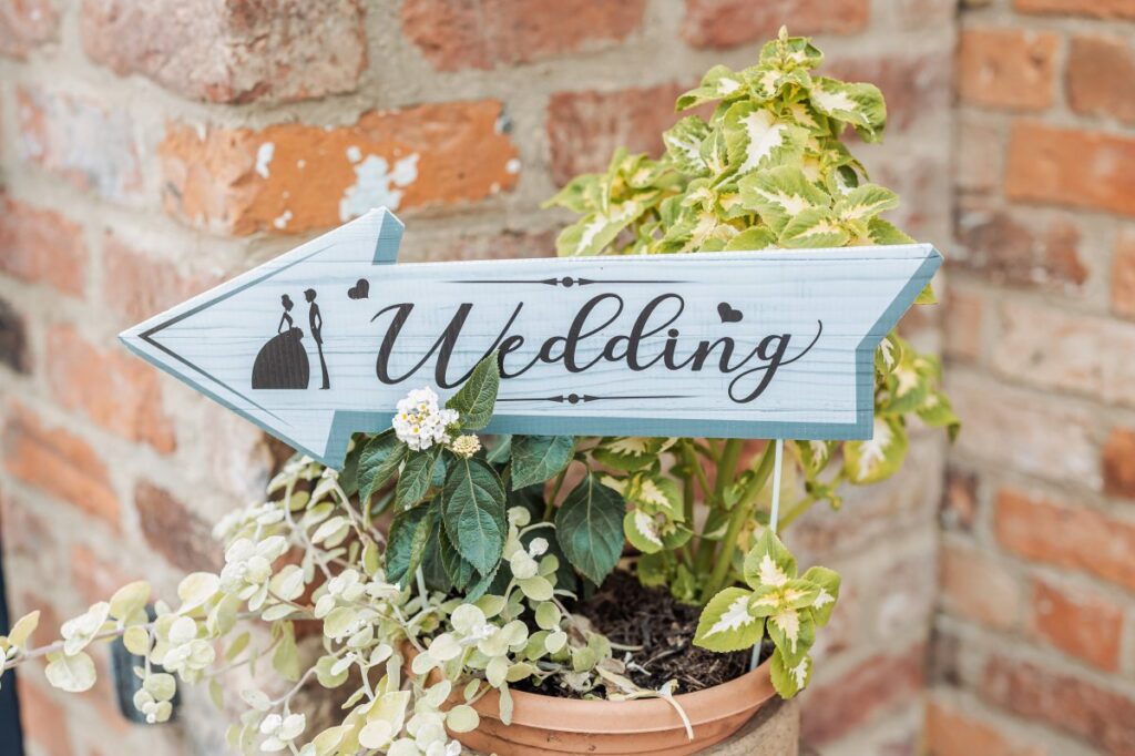 A painted wooden Wedding sign against the red brick of Clayfield Farm.