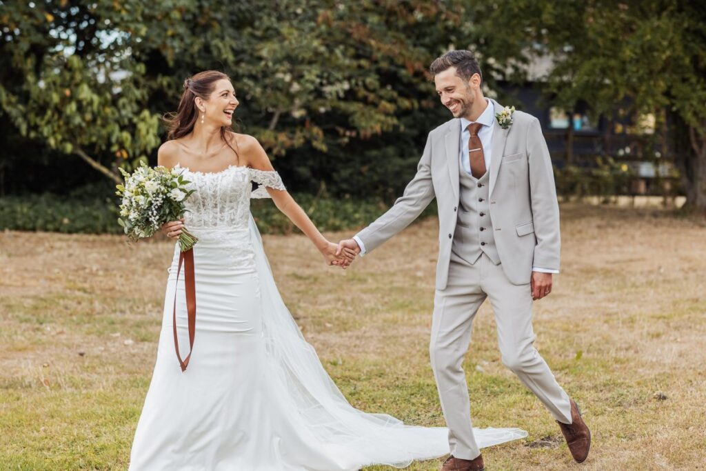 Bride and groom laugh as they walk hand in hand across the lawn on their summer wedding day near York.