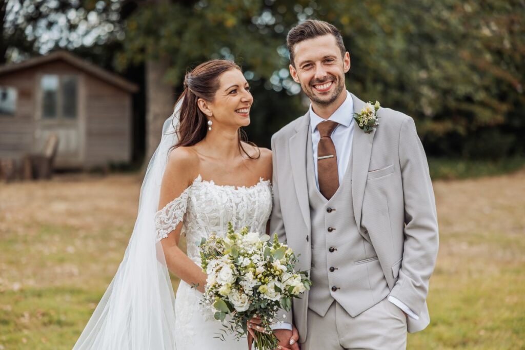 Portrait of the bride and groom at Clayfield Farm, with the farm's timber cabins behind them.